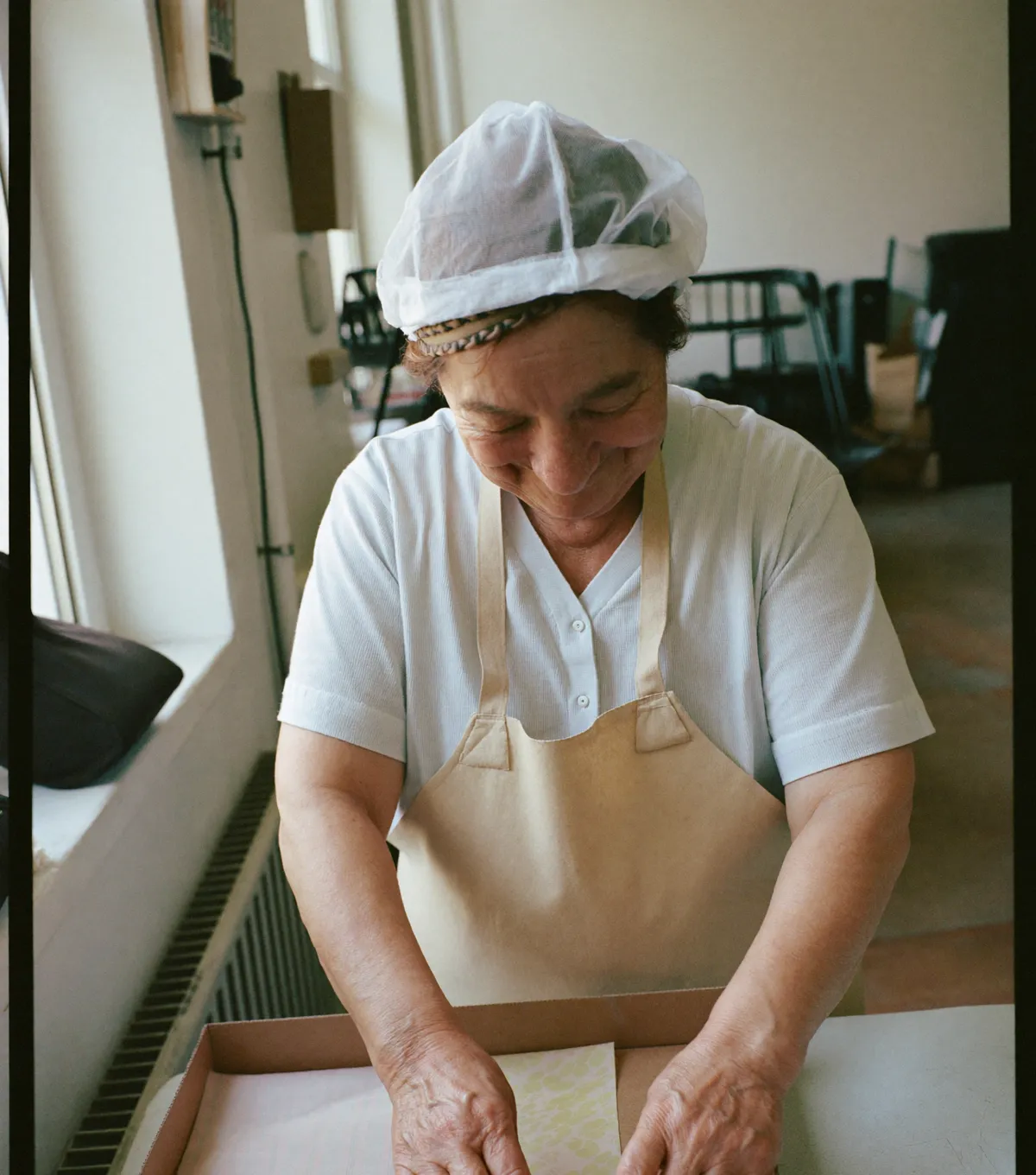 Render of a smiling factory worker in a cream ULAN apron at her workstation
